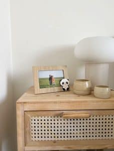 Houtkleurig fotolijstje met schattige panda geplaatst op een houten nachtkastje met rotan front. In de lijst zit een familiefoto van een ouder met kind op een grasveld. Naast de lijst staan twee keramieken kaarsenhouders en een zachte tafellamp, wat de warme sfeer in de kinderkamer benadrukt. De lijst is beschikbaar in 10x15 cm, 13x18 cm en 15x20 cm.