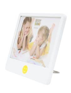 Schuin zijaanzicht van een witte Deknudt fotolijst van 10x15 cm met een gele smiley onderaan. In de lijst zit een foto van twee jonge meisjes die lachend naar elkaar kijken terwijl ze tekenen. De lijst staat stabiel op een metalen standaard.